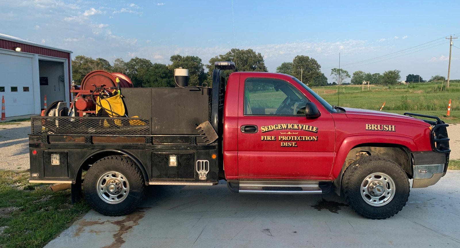 A red brush truck in parking lot next to a fire station